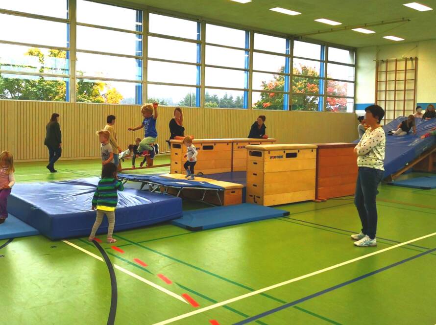 Beispielfoto eines Parkours mit zahlreichen Kindern aus dem Kinderturnen in der großen Turnhalle. Die Gesichter sind verpixelt.